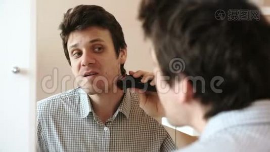 机刮脸发.. 年轻英俊的男人用电动修剪机干剃须刀。视频