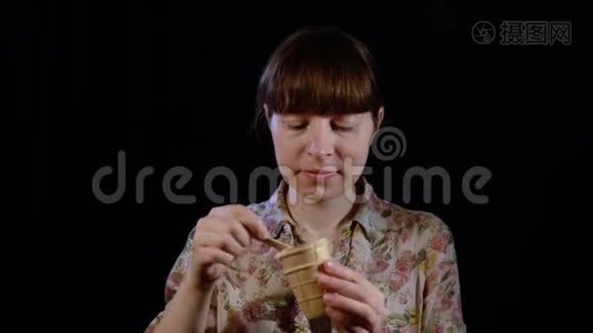 年轻的女人正在用勺子在黑色的背景上吃冰淇淋。视频
