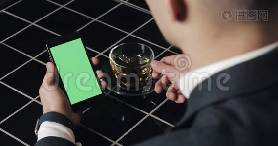 年轻的商人使用带有绿色屏幕触摸板的smarthpone，并在咖啡馆打手势接近。 一个拿着手机的家伙，敲视频