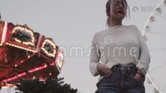 戴眼镜的小女孩站在游乐园的旋转木马附近视频