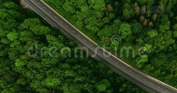 空中景色随着汽车的移动飞越公路，那穿过车道的绿色森林。 汽车沿林路行驶.. 汽车轮胎视频