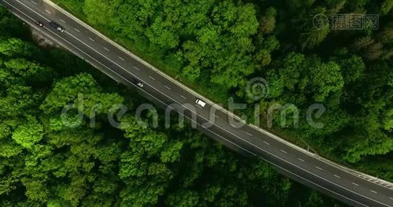 空中景色随着汽车的移动飞越公路，那穿过车道的绿色森林。 汽车沿林路行驶.. 汽车轮胎视频