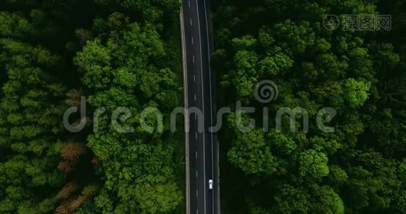 空中景色随着汽车的移动飞越公路，那穿过车道的绿色森林。 汽车沿林路行驶.. 汽车轮胎视频