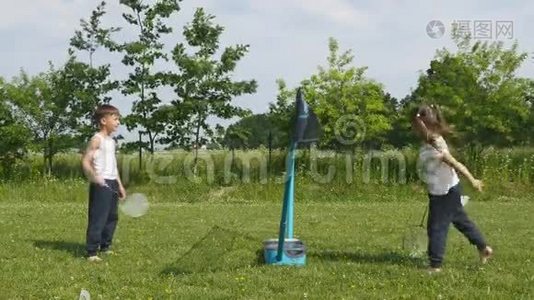 青少年男孩和女孩在草地上打羽毛球，背景是森林。 手持羽毛球拍的儿童视频