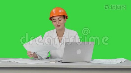 微笑的女工程师与坐在桌子上的相机交谈，在绿色屏幕上有很多文件，Chroma键。视频