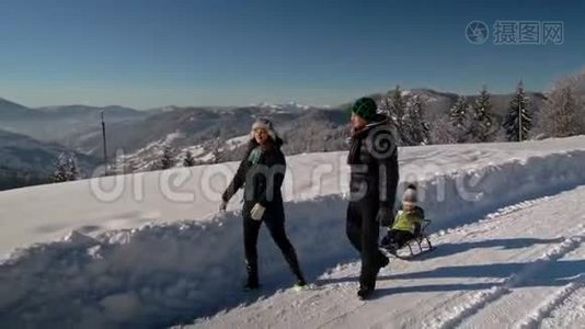 年轻的幸福家庭在雪林里玩得很开心。 父母把他们的小儿子卷在雪橇上。 慢动作。视频