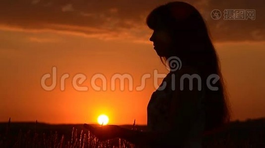 女孩手里拿着夕阳，女孩的剪影在夕阳的背景下。视频