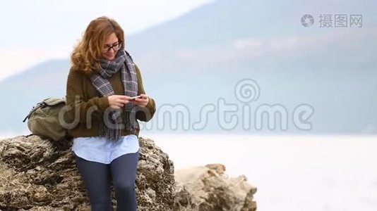 一个背着背包的女旅行者站在海上的岩石上视频