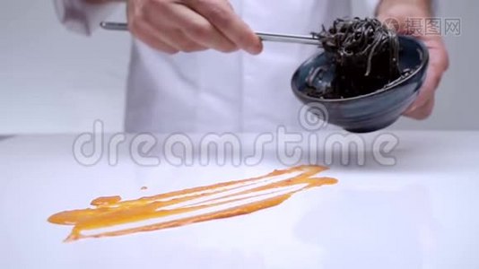 厨师的手铺在一张白色的桌子上，上面有奶油黑色的意大利面。视频