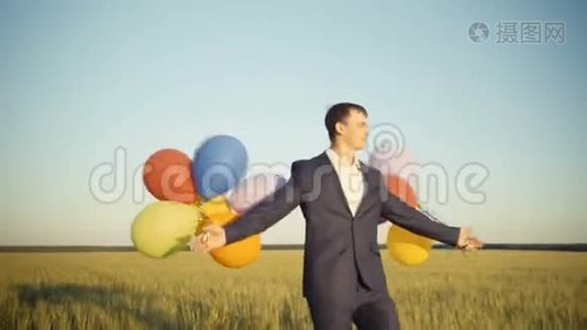 创意商人手持五颜六色的气球在一个田野散步。视频