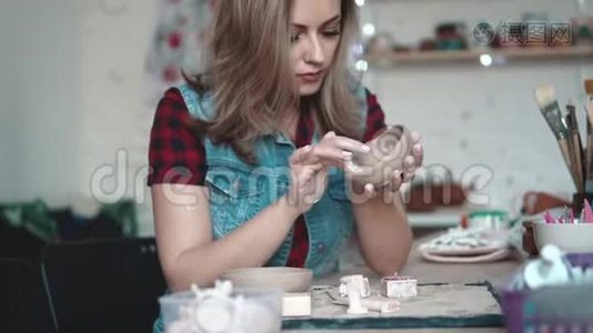 年轻的女人在车间里创造了一盘粘土。 女孩手里拿着一种形状的粘土。 创造性爱好视频