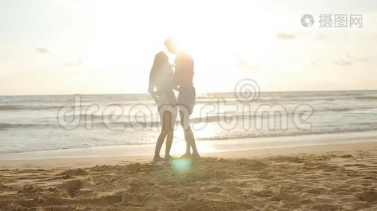 年轻夫妇在海滩上，男人拥抱和旋转他的女人在日落。 男朋友把女孩抱在怀里，旋转着她视频