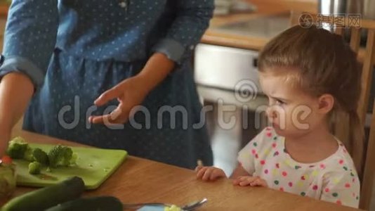 厨房里的小女孩和她妈妈在一起。妈妈给了西兰花的女儿。女孩坚决地拒绝视频