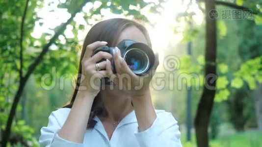 一位身穿白衬衫、笑容可掬的女摄影师正在公园里柔和的背景下拍摄照片视频