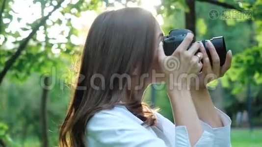 一位身穿白衬衫、笑容可掬的女摄影师正在公园里柔和的背景下拍摄照片视频