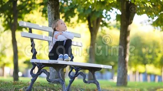 可爱的孩子坐在美丽的秋日户外失去了思考。 小女孩倒在长凳上视频