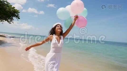 快乐的漂亮女孩穿着白色连衣裙在海滩上奔跑，手里拿着气球跳跃。 慢动作。 概念幸福视频