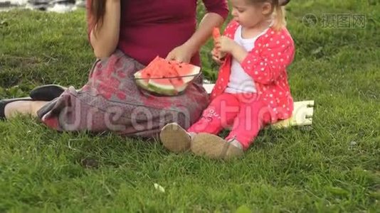 母亲和女儿在夏天在海边野餐吃西瓜。视频