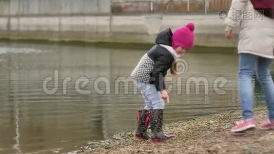 母亲和她的小女儿，沿着石滩散步，收集贝壳，把石头扔进水里视频