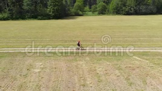 空中：男子骑自行车沿着乡间小路穿过耕地和农田，阳光明媚的一天，环保的交通运输视频