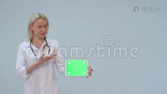 一位女医生的肖像，白色外套和绿色屏幕的平板电脑视频