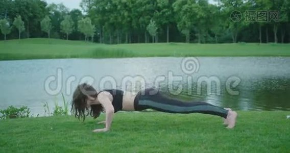 这位身材苗条的女士正在河边做俯卧撑。视频