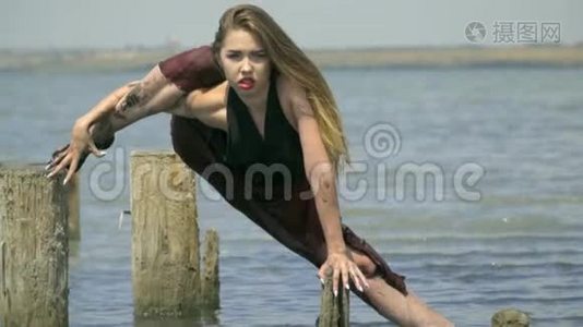 一个穿着湿衣服的肮脏的金发女郎站在河口，一只脚靠在一个废弃盐池的木柱上视频