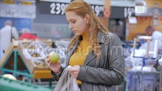 漂亮的年轻漂亮的红发女人在市场上，在超市里买食物、水果、苹果。 女孩选择视频