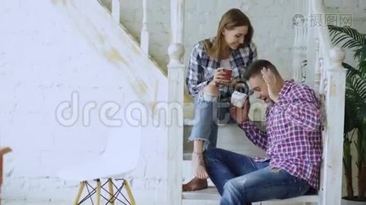年轻、快乐、可爱的一对夫妇在家中坐在楼梯上喝茶聊天视频