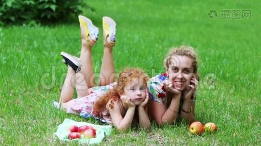可爱的红头发的小女孩和她的母亲躺在草坪上视频