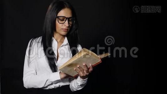 肖像吸引人的女人读书。 美丽的年轻黑发，长发，穿着白色衬衫，摆在工作室里视频