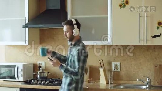 一个英俊的年轻人戴着耳机在家里的厨房里跳舞唱歌，在假期里玩得开心视频