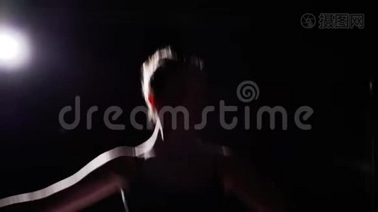 优雅的芭蕾舞演员在她的尖角芭蕾舞鞋上跳舞，在演播室的黑色背景上聚光灯下。 女人表演经典节目视频
