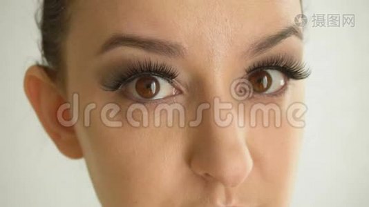 长着假睫毛和棕色眼睛的女性脸看着相机。 化妆时尚的特写美女模特视频