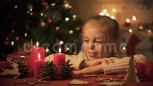 小女孩看着桌子上的圣诞装饰品，树上的灯光闪烁视频