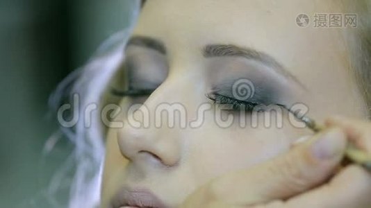 专业化妆师用眼笔和画笔在金发模特眼皮上做眼睑箭头。视频