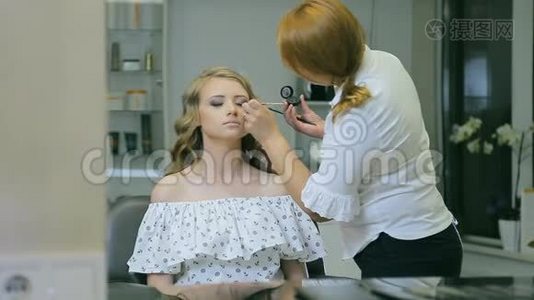 专业化妆师用眼笔和画笔在金发模特眼皮上做眼睑箭头。视频