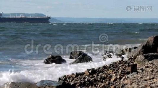 海浪拍打着海岸上的岩石，背景上的货船视频
