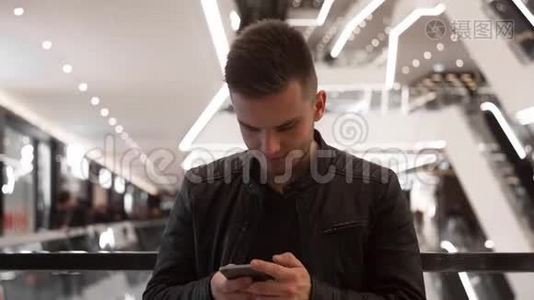 年轻人站在购物中心，用智能手机。视频