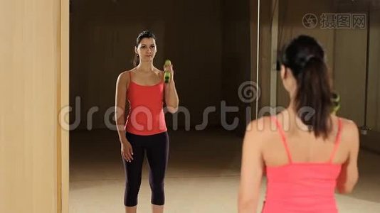 运动的女人用哑铃抬高肌肉。 健身模特照镜子。视频