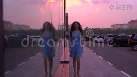 苗条的黑发女孩，穿着蓝色连衣裙，在粉红色日落天空的街道上散步，4K视频视频