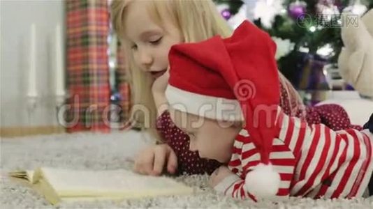 戴着圣诞帽的女孩和男孩在圣诞树前看书。视频