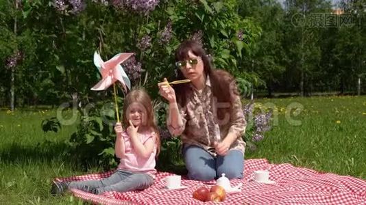 年轻的母亲和小女儿在春天的野餐旁边，一朵盛开的丁香花。视频
