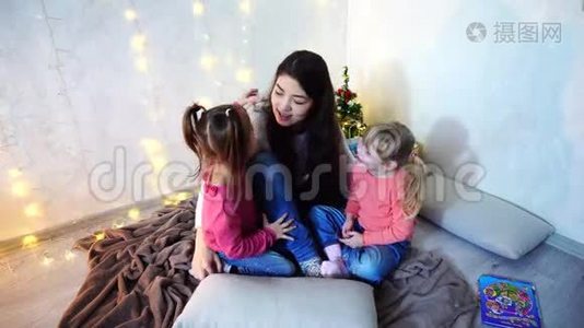 美丽的姐姐，在圣诞树和圣诞树的背景下，和坐在地毯上的小女孩玩耍视频