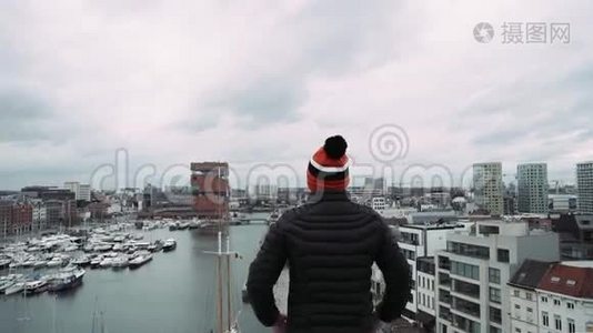 年轻的帅哥在工业城市景观背景下的摩天大楼屋顶上举手。视频