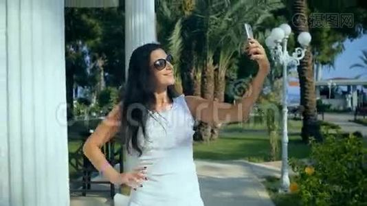美丽快乐的年轻女人在夏天的公园里用智能手机在户外自拍。视频