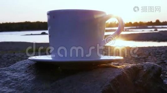 一杯带烟的红茶，站在河边的一块岩石上，看着金色的夕阳，在水面上闪闪发光。 高清高清视频