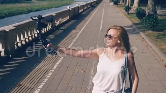美丽快乐的女博主带着相机，领着她的报告文学漫步在度假城市的堤岸上。这个视频