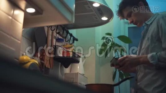 男人在厨房的炉子上用锅做饭，用平板电脑视频