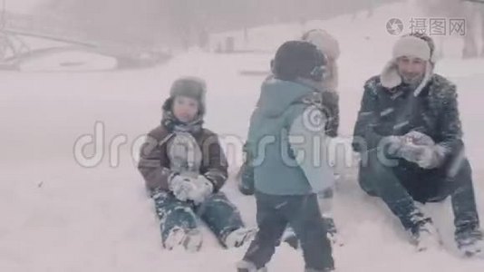 一家人坐在雪地上。 妈妈做雪球。 爸爸和一个孩子说话。视频
